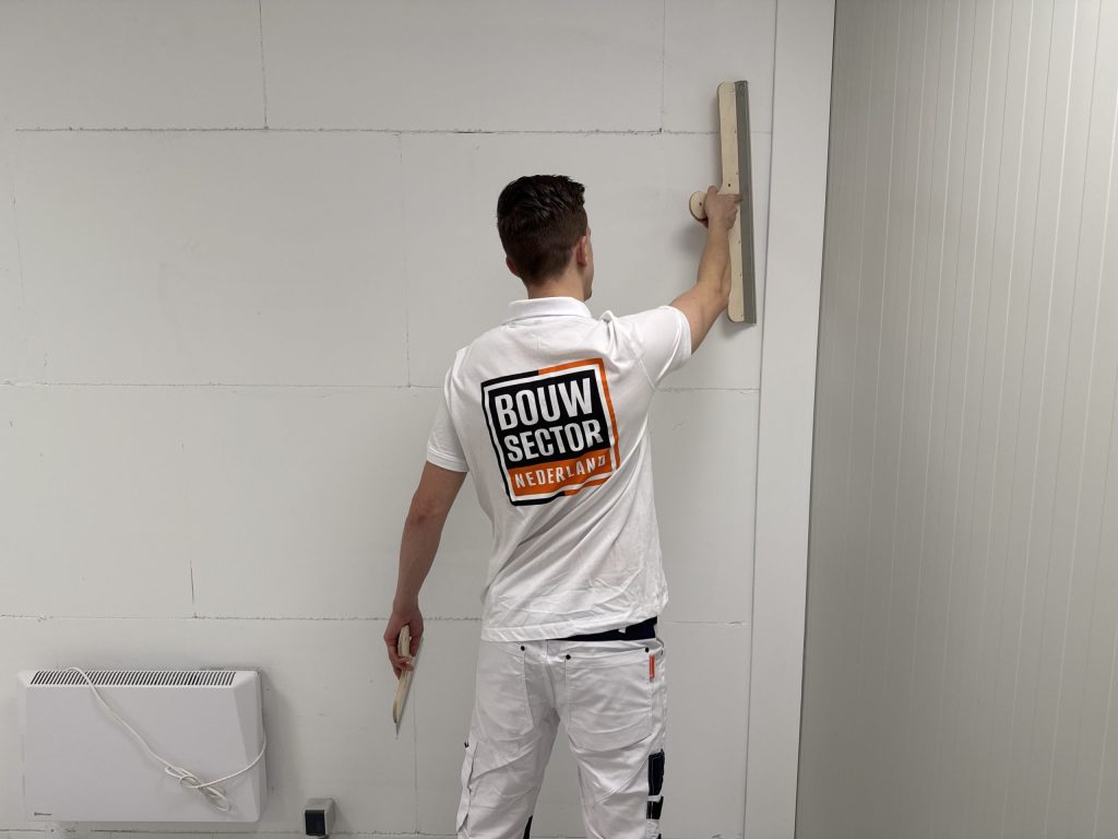 Vakman van Bouwsector Nederland trekt een brede spaan omhoog langs een witte wand